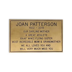 A rectangular brass memorial plaque with an engraved message, personalized text, and a gold-colored border.