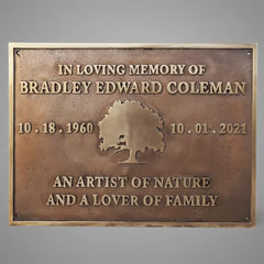 Bronze memorial grave plaque engraved with engraved text and tree design on a gray background