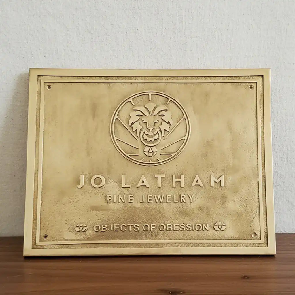 Engraved brass address sign | Brass plaque with logo and text on a wooden surface.
