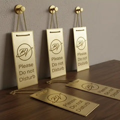 Brass metal tag with engraved signs on a wooden surface and wall.