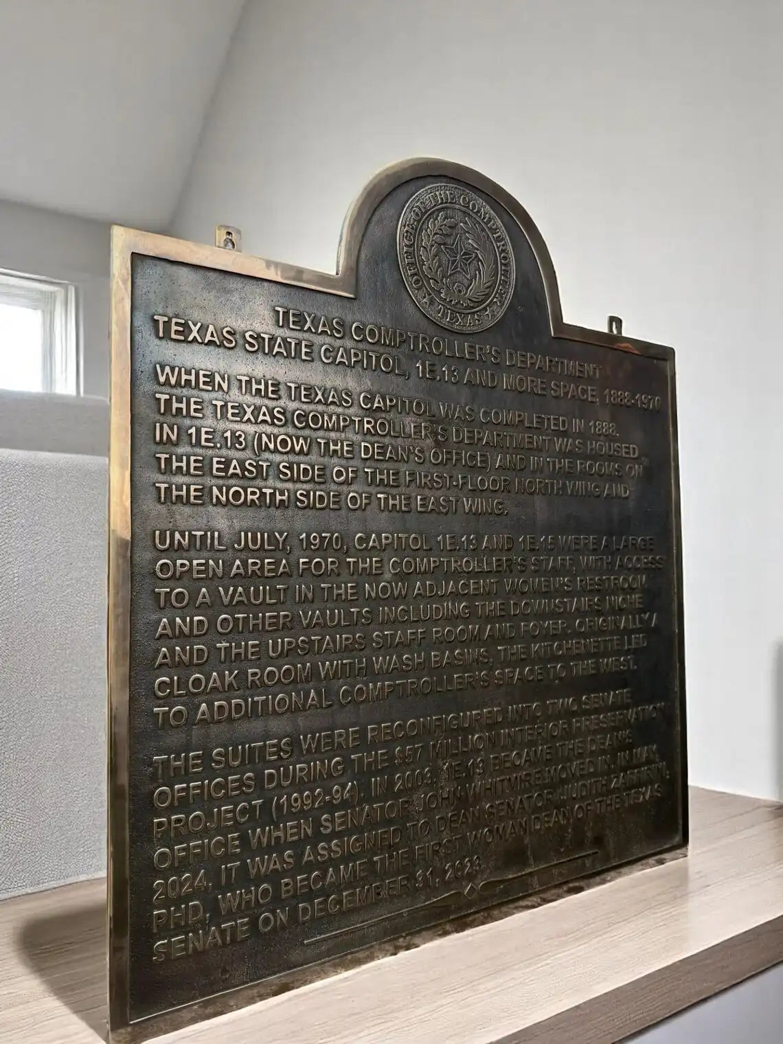 Bronze plaque with engraved text on a wooden stand against a neutral background