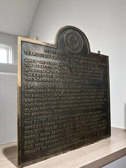 Bronze plaque with engraved text on a wooden stand against a neutral background