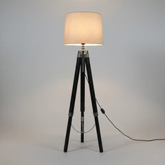 Floor lamp with a beige shade on a tripod base against a gray background