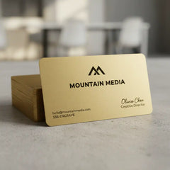 Gold business cards with 'Mountain Media' branding on a blurred indoor background