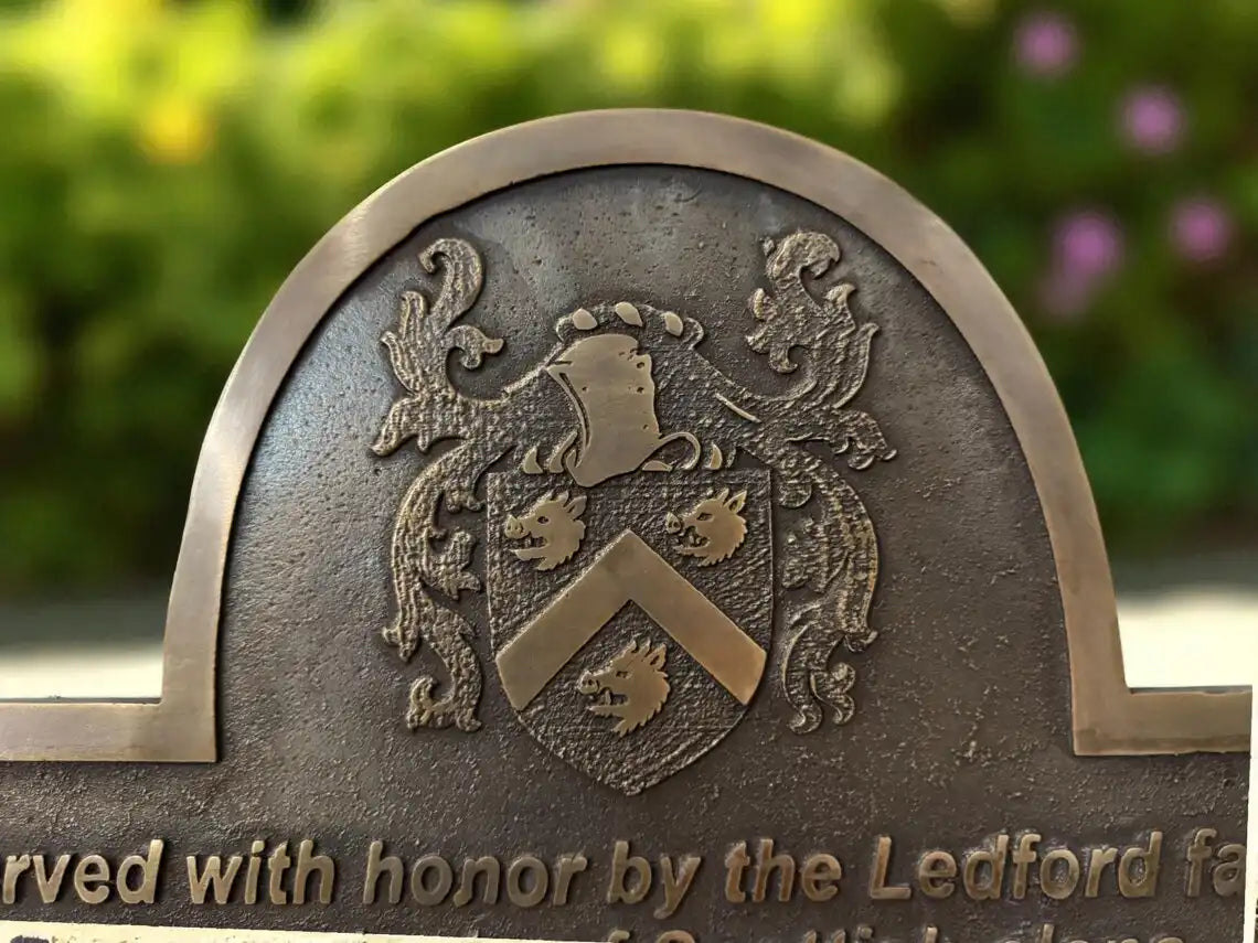Bronze plaque with heraldic design and engraved text against a blurred natural background