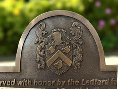 Bronze plaque with heraldic design and engraved text against a blurred natural background