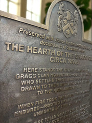 Bronze plaque with engraved text and family crest, set against a blurred indoor background.