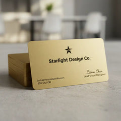 Gold business cards and a brass label plate on a blurred indoor background