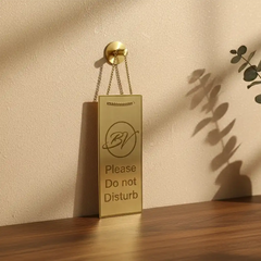Small brass equipment tag—a gold 'Please Do Not Disturb' sign on a wooden surface with a beige wall background