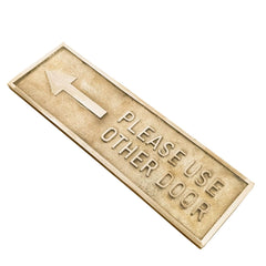 Angled view of the "Please Use Other Door" brass plaque showing engraving depth and shine