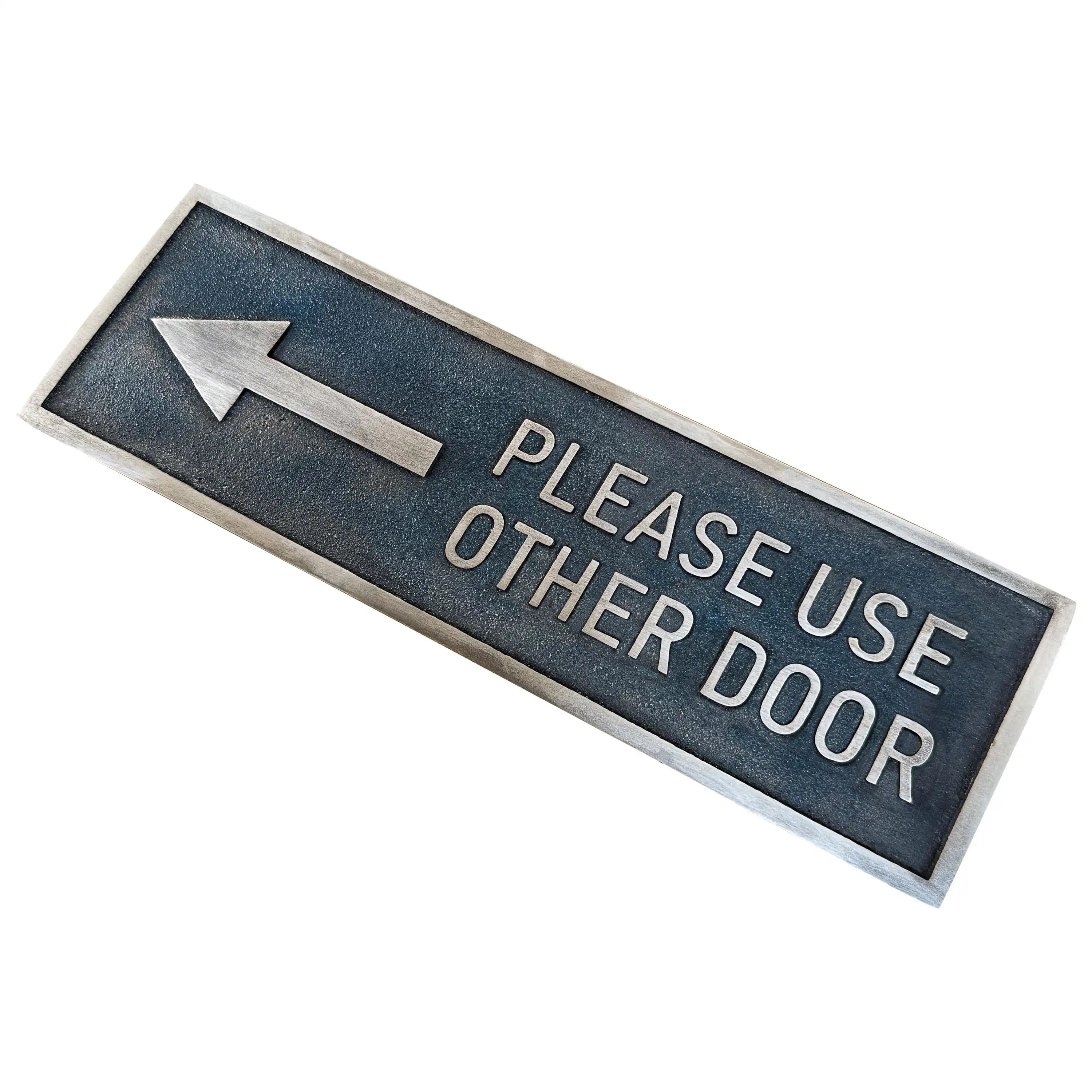 Angled view of the "Please Use Other Door" bronze plaque showing engraving depth and shine