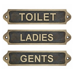 Three brass signs labeled 'TOILET', 'LADIES', and 'GENTS' on a white background.