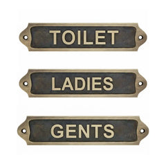 Three brass signs labeled 'TOILET', 'LADIES', and 'GENTS' on a white background.