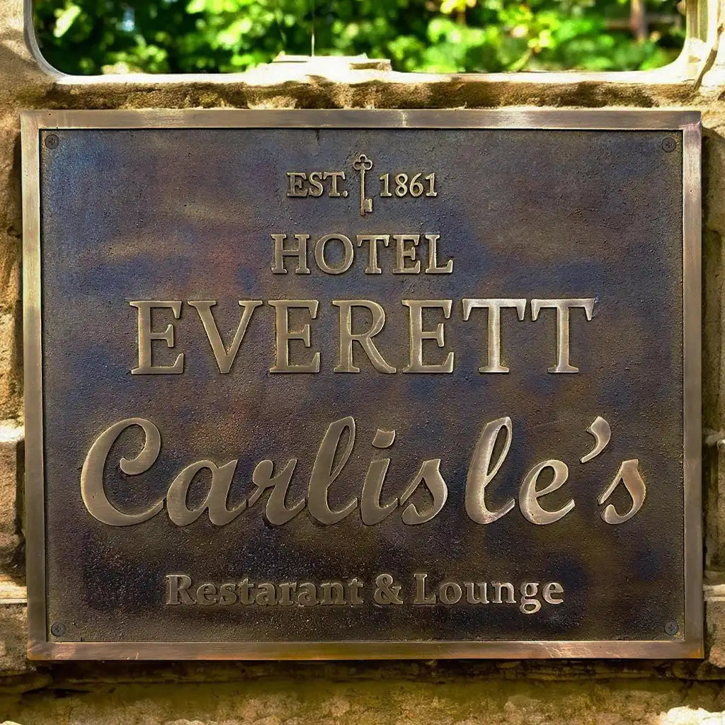 An aged bronze plaque sign, a metal plaque with 'Hotel Everett Carlisle's' text on a stone wall.
