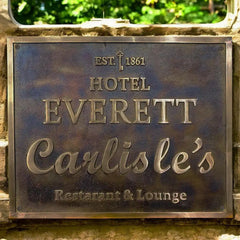 An aged bronze plaque sign, a metal plaque with 'Hotel Everett Carlisle's' text on a stone wall.